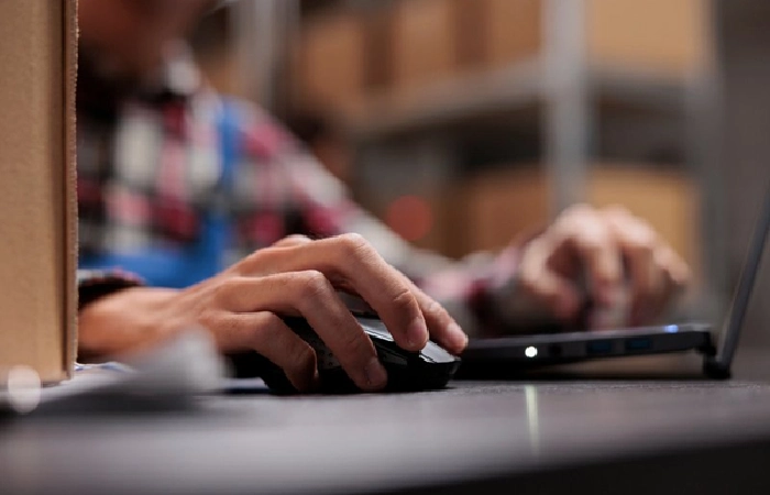 Warehouse worker managing online orders using a laptop and computer mouse